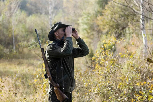 Hunter using binoculars carrying a rifle for ten outdoor survival hacks you might need.